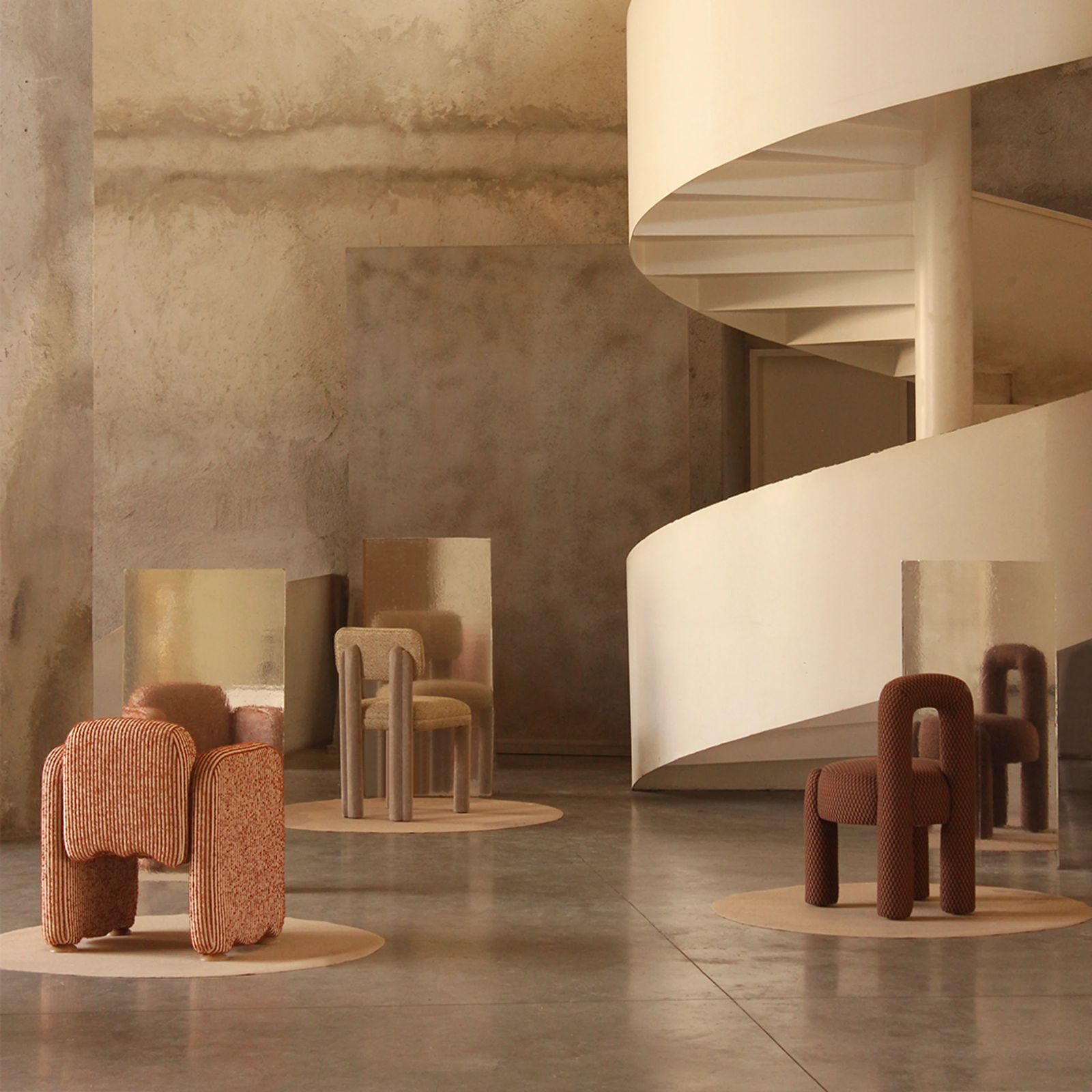 Sculptural upholstered chairs arranged beside a white spiral staircase